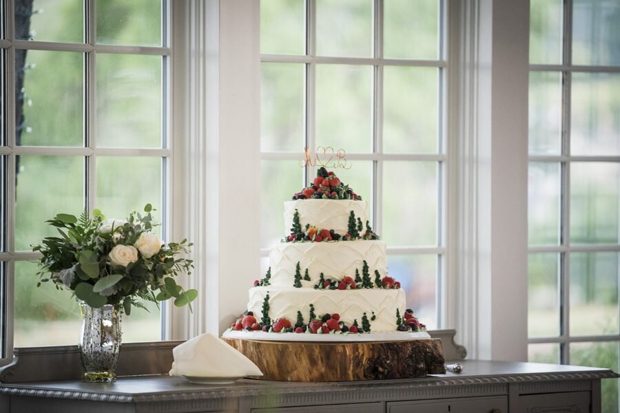 A three-tier wedding cake with white icing, berries, and green icing to look like evergreens.