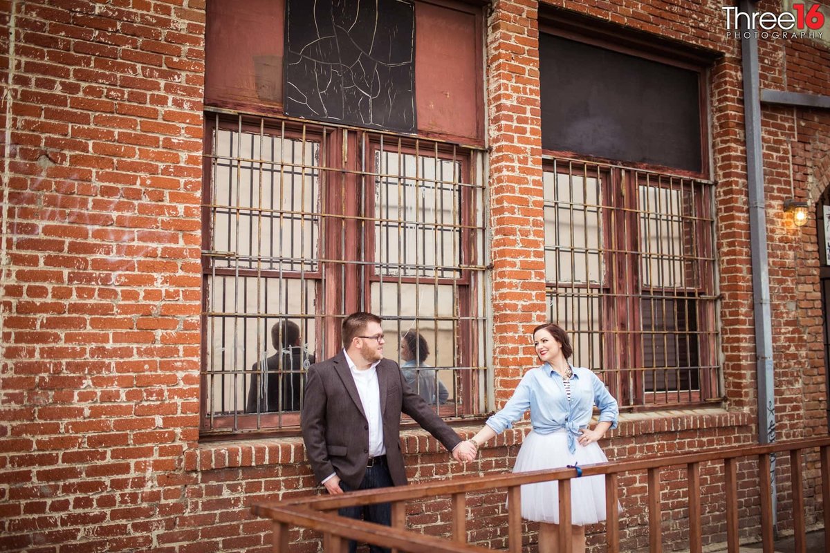 Engaged couple hold hands standing in front of a brick building