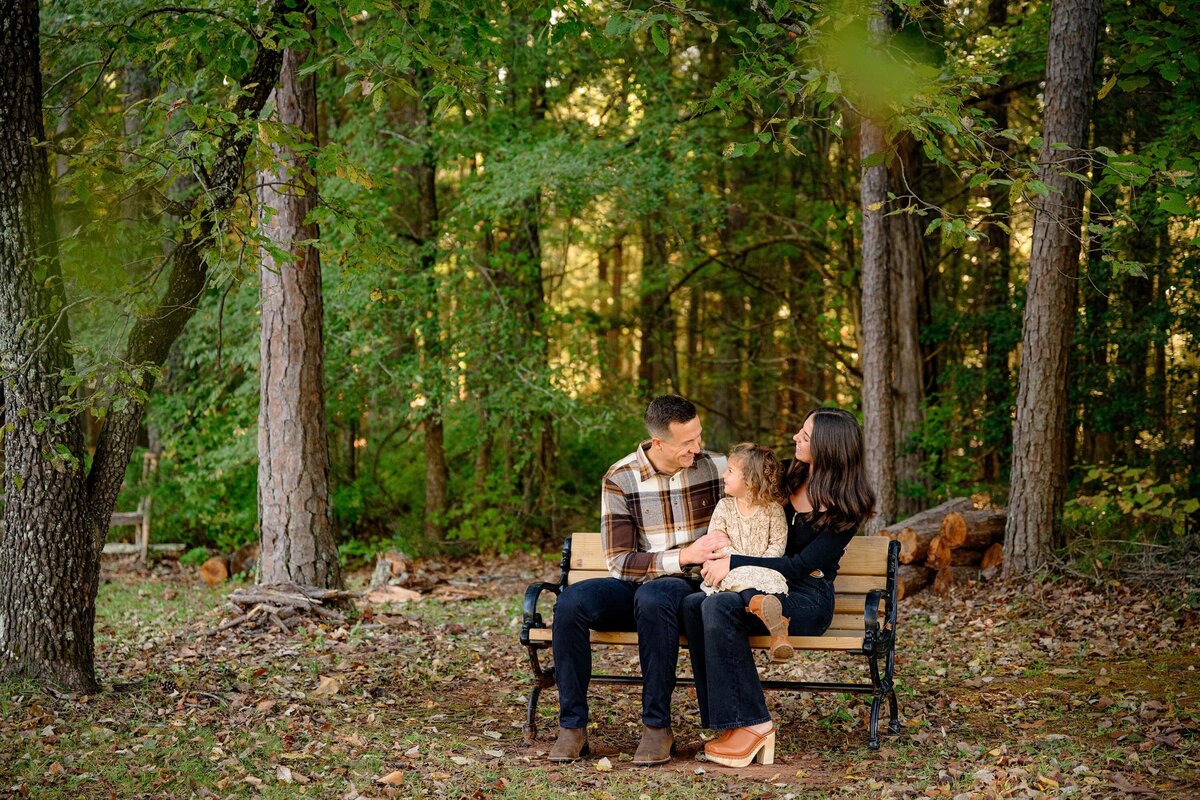family of three sits on a bench in a wooden landscape in lancaster, sc