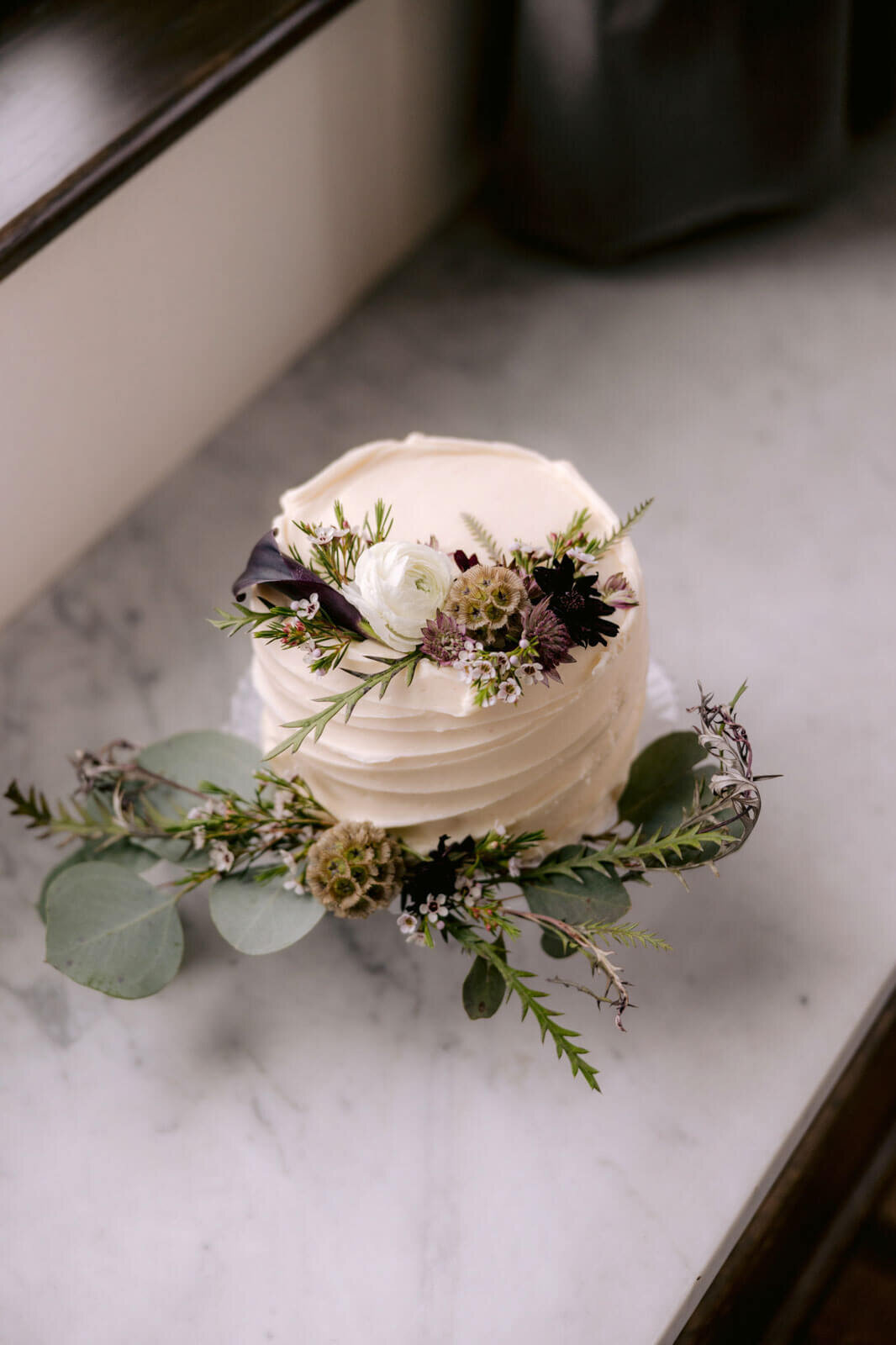 A small white wedding cake with flowers and leaves on top and at the bottom.