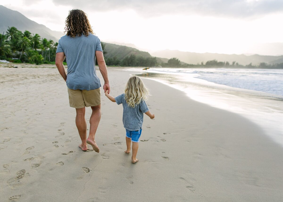 A man holds the hand of his little son along the beach of Kauai.
