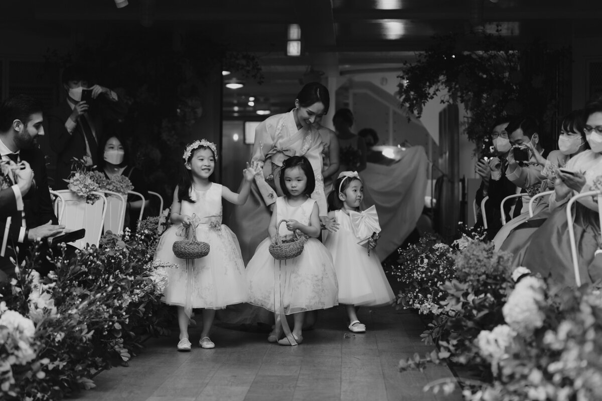 little flower girls walking down the aisle while wearing their little white dress while holding a basket full of flower petals
