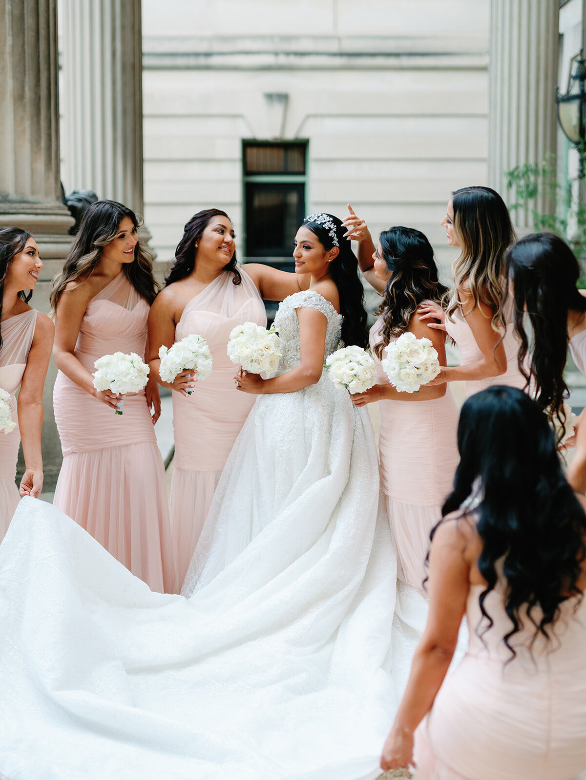 Bride and bridesmaids share a moment together in front of the wedding venue.