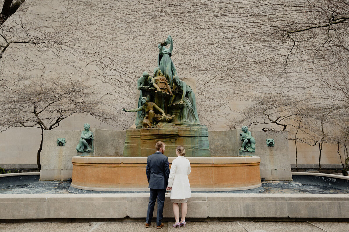 Just Married photo session couple stands and looks at fountain statue in the Art Institute Garden Chicago