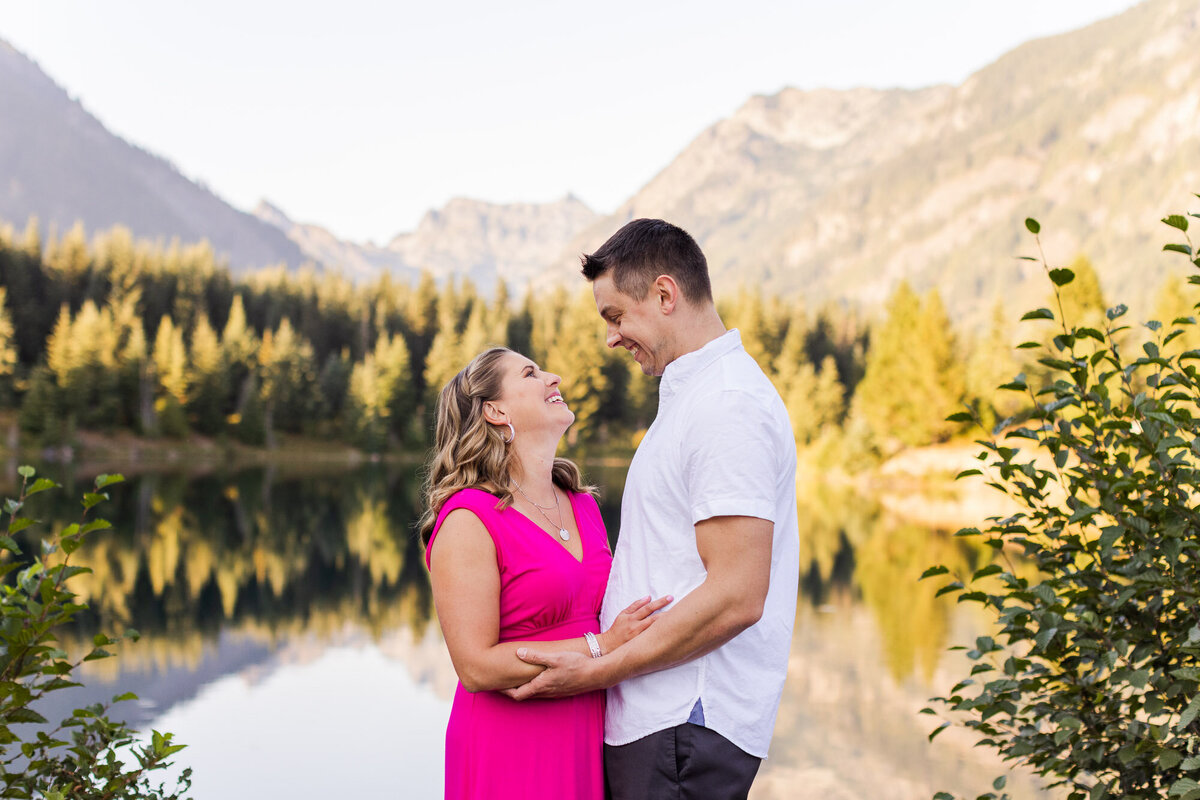 PNW engagement session at Gold Creek Pond near Seattle happy couple smiling with colorful lake and mountain view candid photo by Joanna Monger Photography