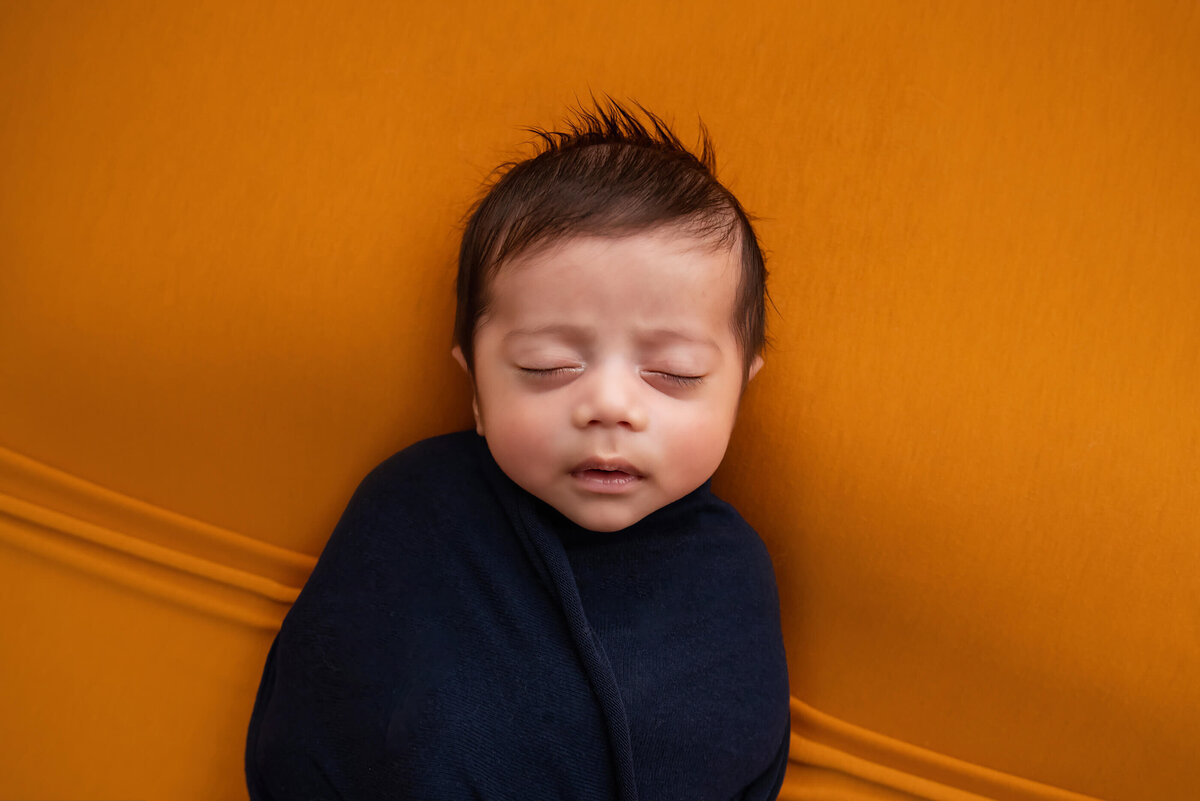 up close photo of baby wrapped in blue on an orange background for his newborn photos