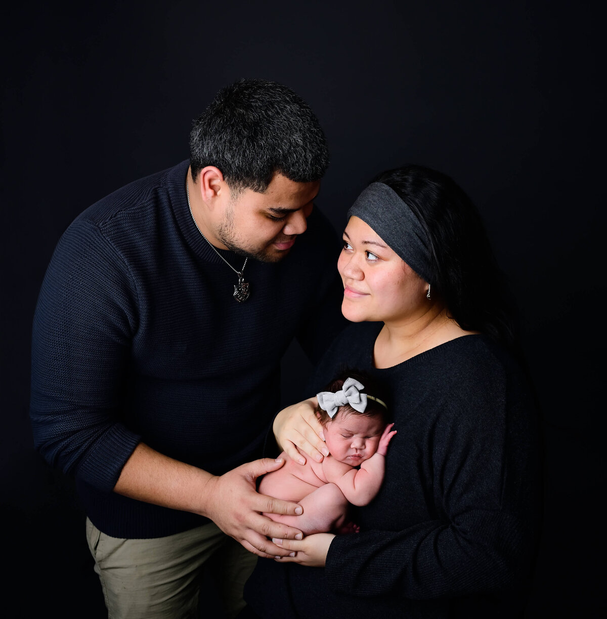 A mother and father looking at each other while holding their newborn daughter during their newborn photo session. Image captured by E. Benecki Photography of Kitsap County, WA
