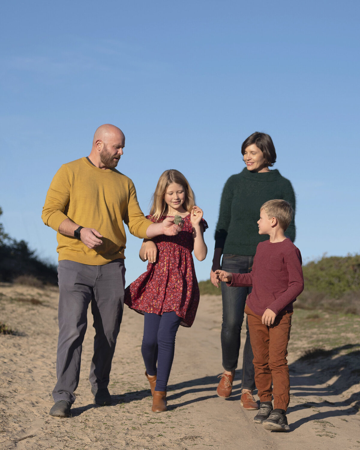 Family of four walking on a trail outdoors with bright blue sky behind them. Captured by San Francisco Family Photographer