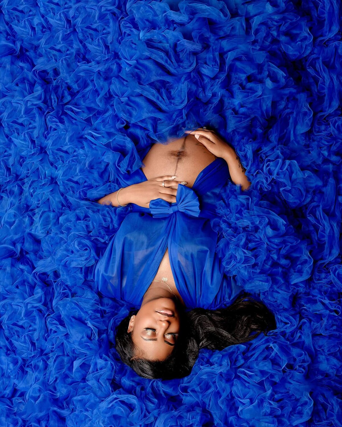 Portrait of mother laying down on her back with fabric all over  with hands on her growing baby bump.