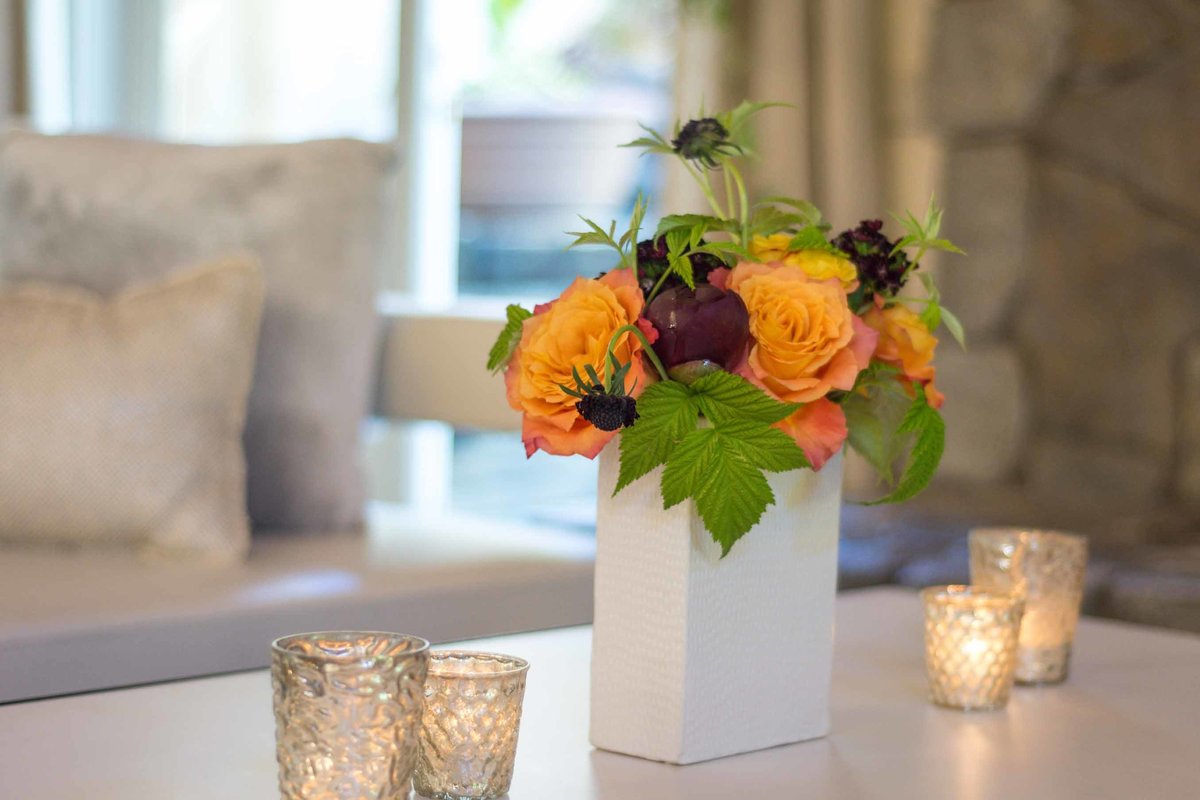 flower arrangement of orange roses in square white vase and silver votives