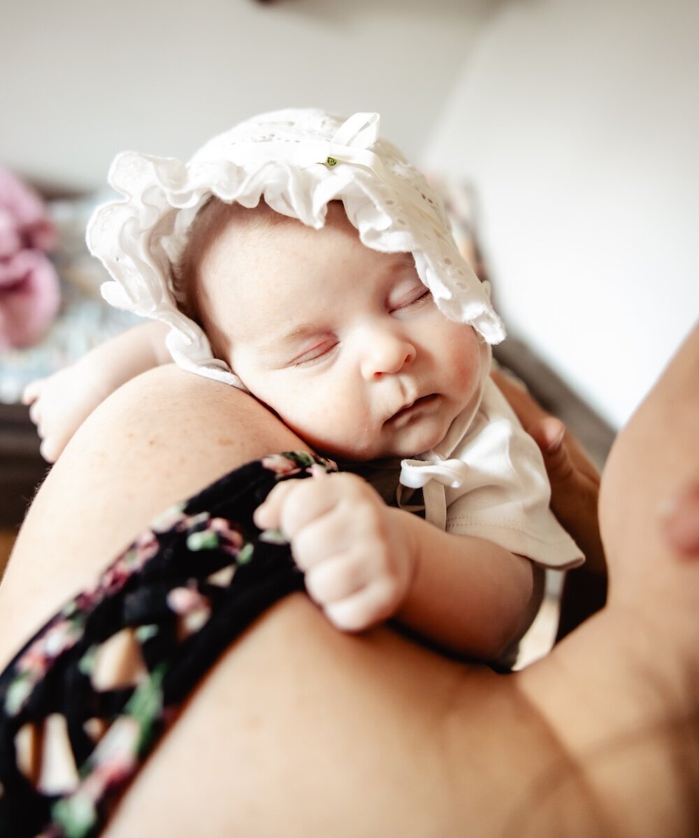 a baby girl wearing a bonnet sleeping on her mother's shoulder