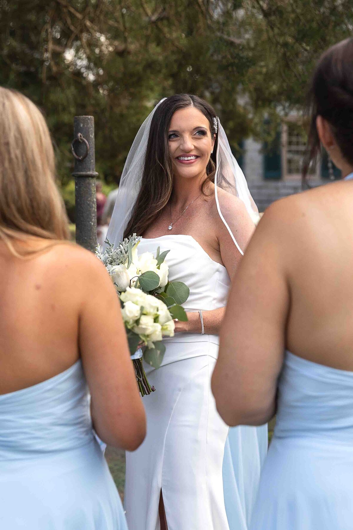 Bride smiling at bridesmaids holding wedding bouquet