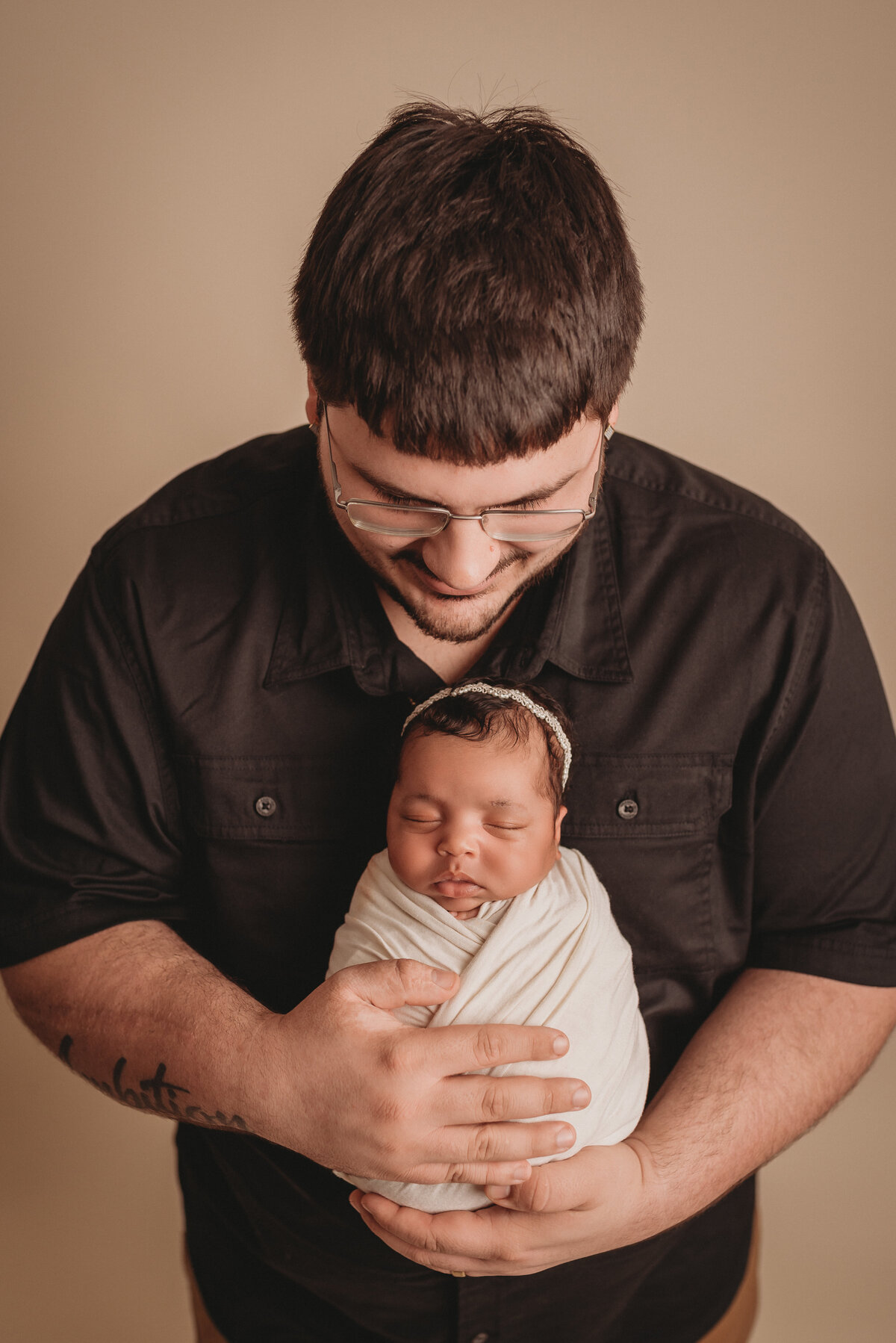 Newborn portraits at Marietta, GA newborn photography studio with dad and baby girl wearing black and creams on a tan backdrop