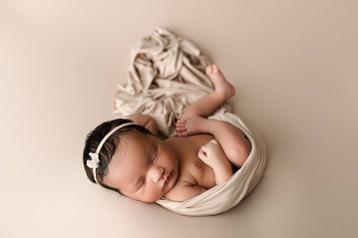 Newborn girl with bow swaddled in tan swaddle studio