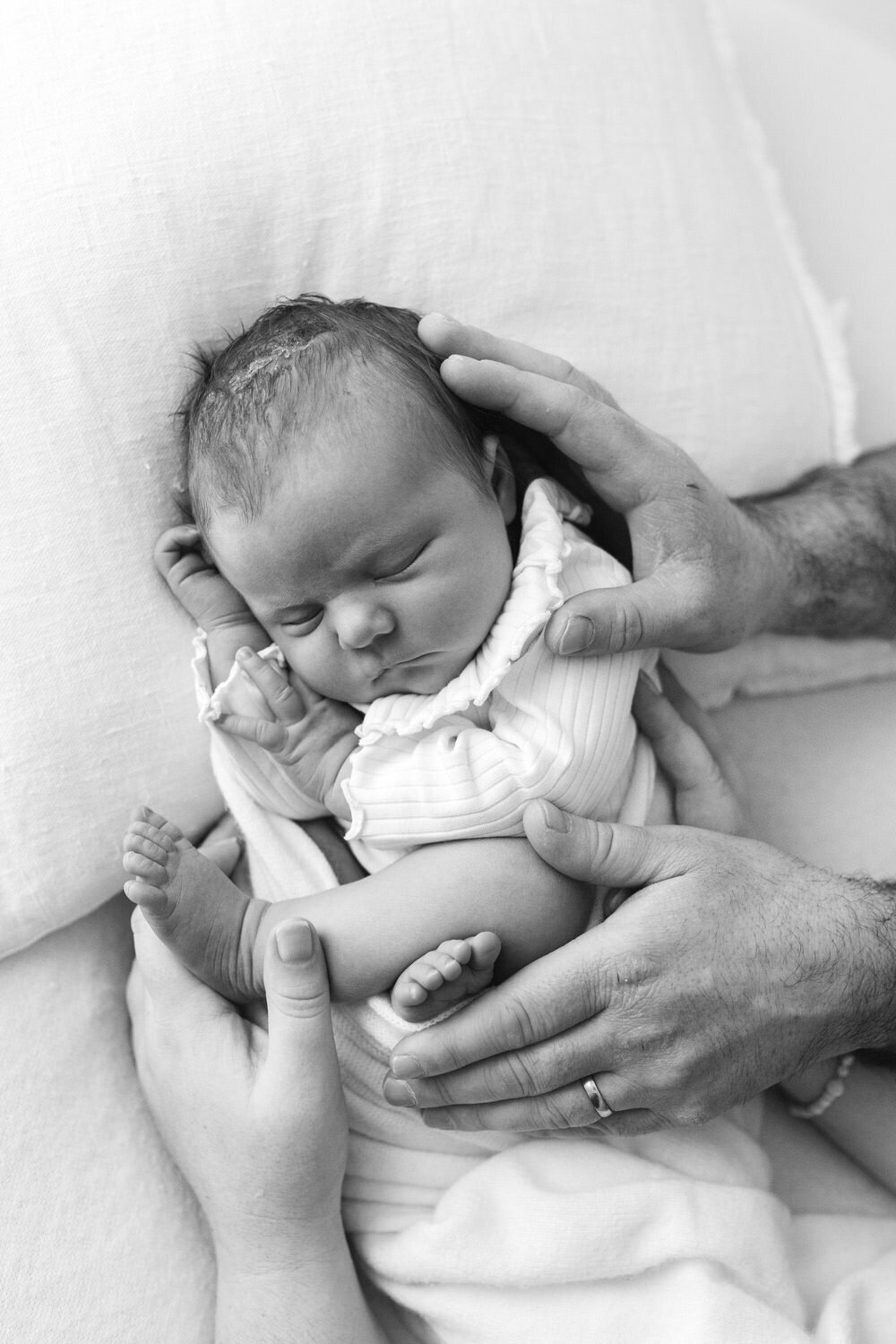 Baby fast asleep held in mum and dads hands, black and white photograph