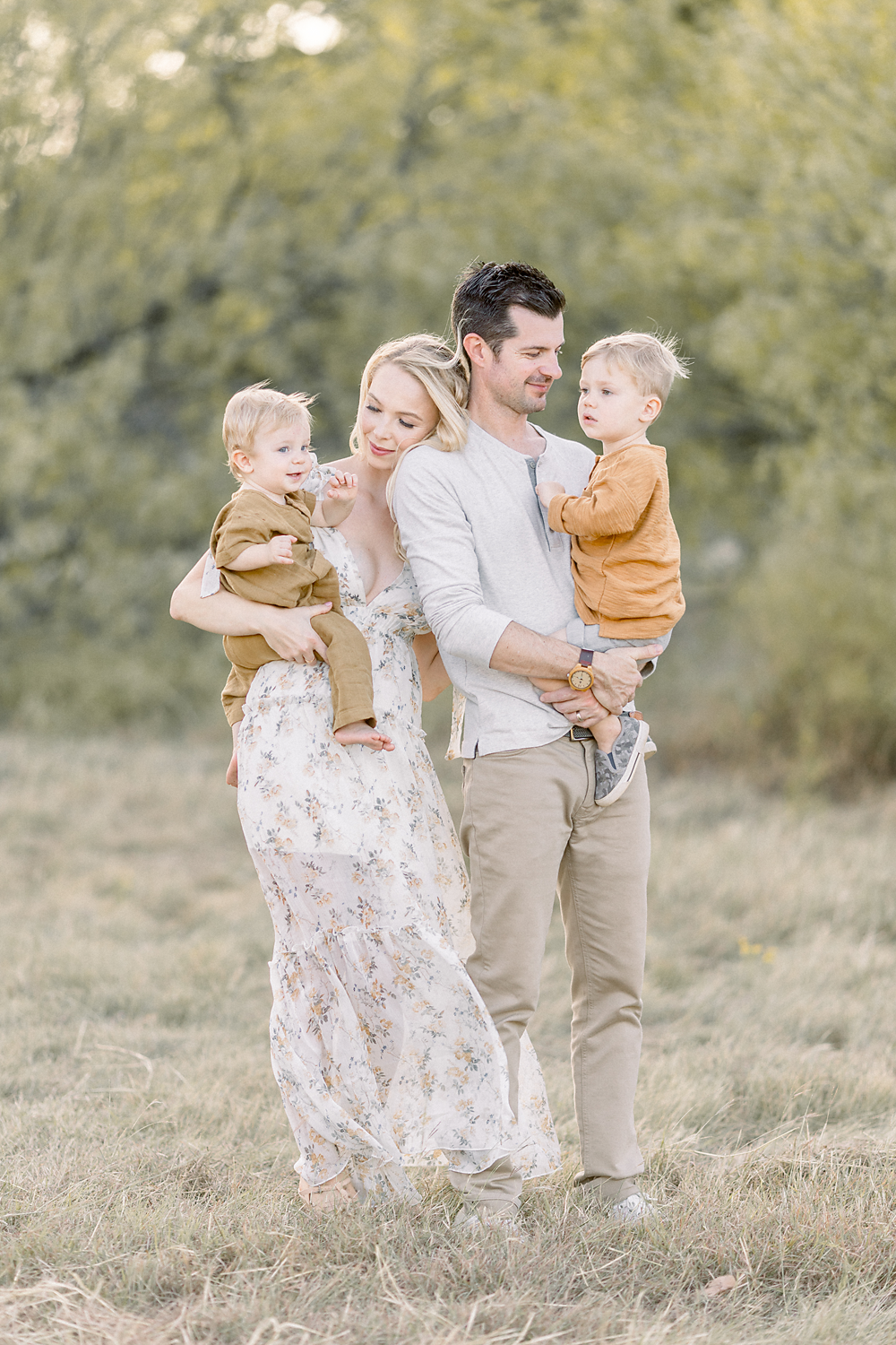 A beautiful family of 4 portrait taken while they are standing together in a field at a local Fort Worth park taken by a family photographer in Dallas TX.