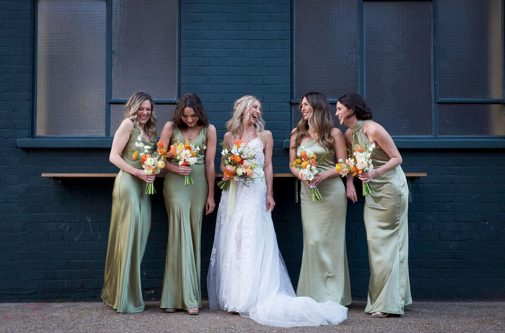 Bride and bridesmaids wearing green sating bridesmaids dresses outside The Hackney Co.