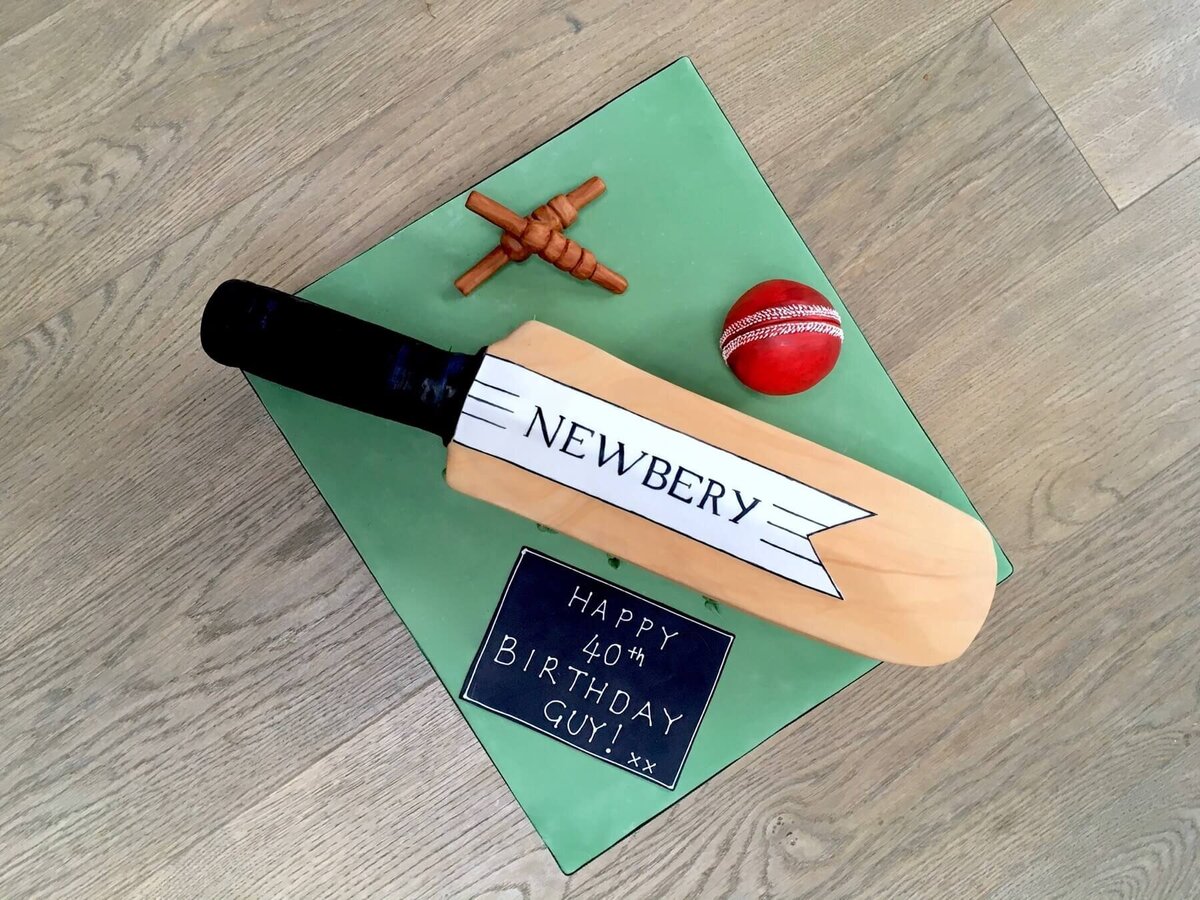 A birthday cake in the shape of a cricket bat, wickets and ball