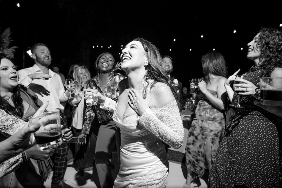 Black and white photograph of a bride singing lyrics to a song with her hand on her chest and eyes closed during her wedding reception at The White Home in Rock Hill, SC