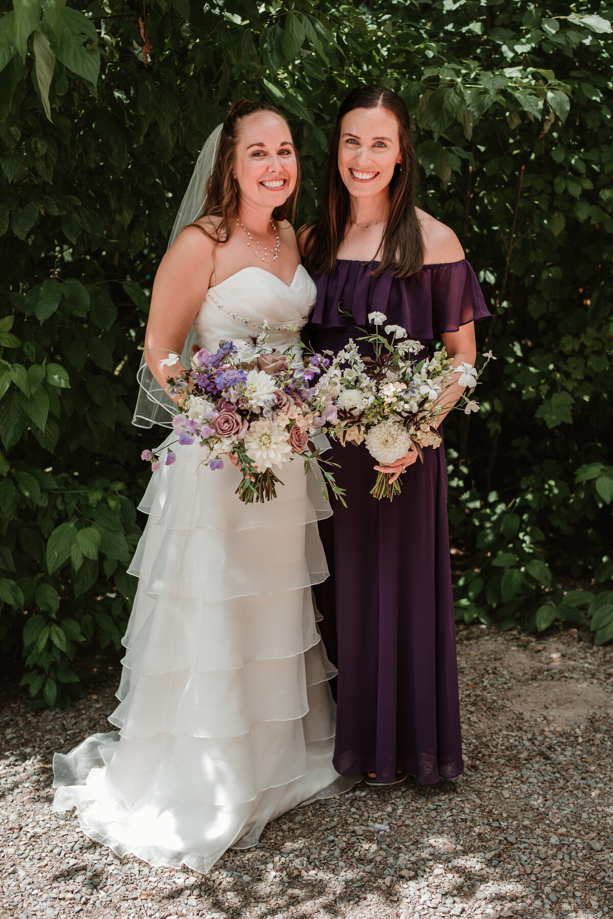 Bride and bridesmaid holding garden-style bouquets with white dahlias, lavender roses, sweet peas, and scabiosa. Designed by Indigo & Violet Co., a Bozeman Montana wedding florist specializing in romantic, airy florals. 