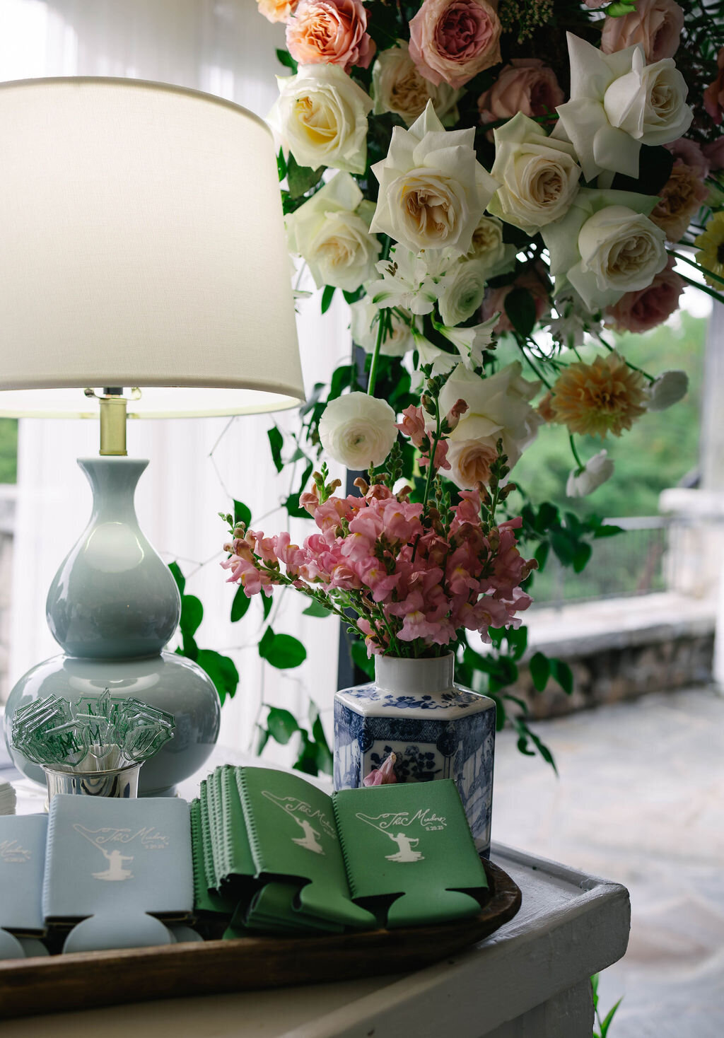 Welcome table with pastel florals, custom monogrammed koozies, and soft blue-green accents at The Bascom Center wedding in Highlands NC.