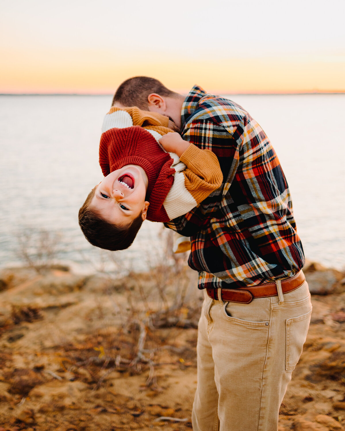 Family photo sessions in Albuquerque capture a playful moment between a father and his son by a beautiful lake. The father is actively engaging with the boy in a game, highlighting the joy and bonding shared during their time together