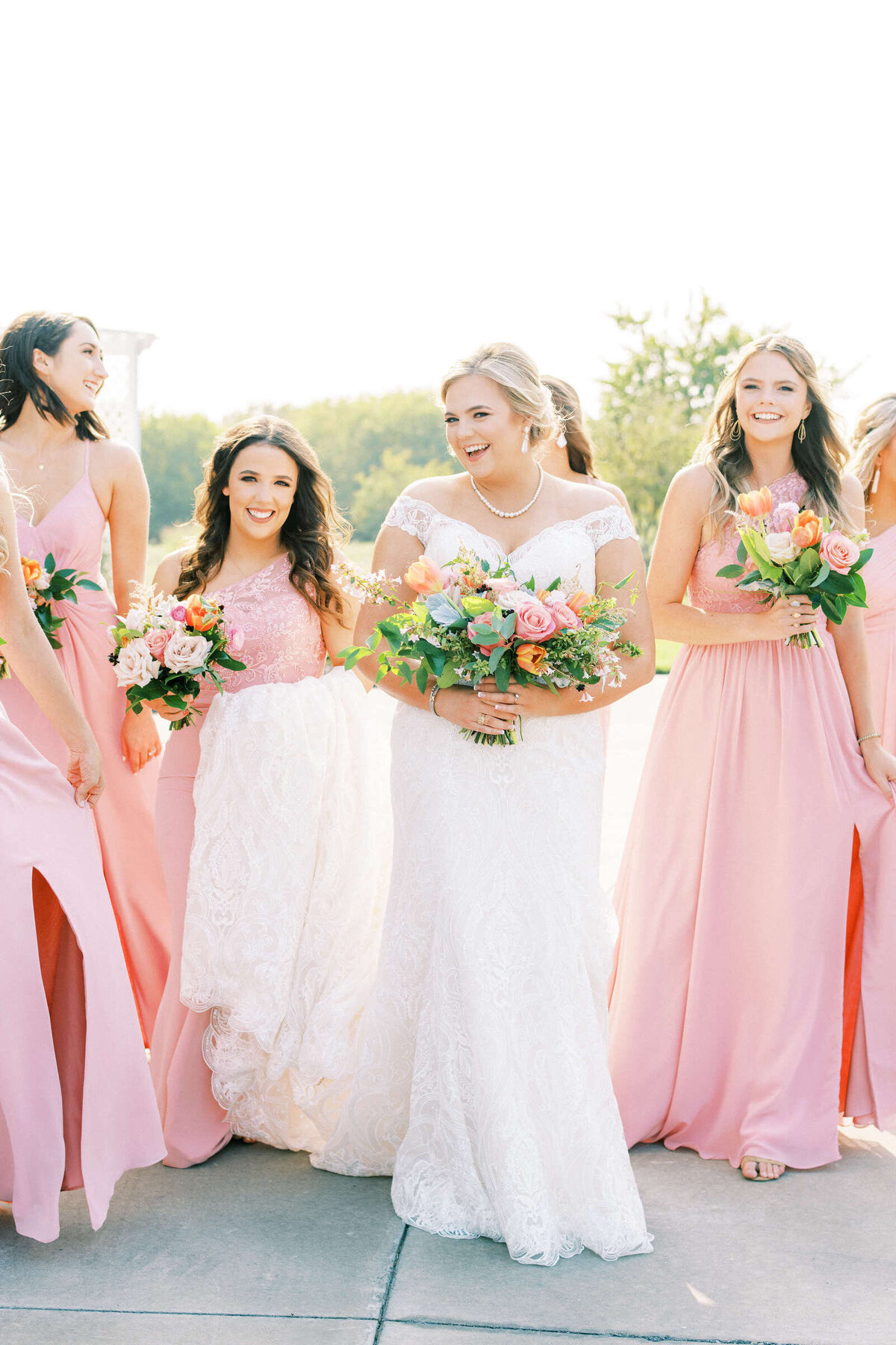 Joyful bridal party in blush dresses smile with bride at summer wedding in North Texas