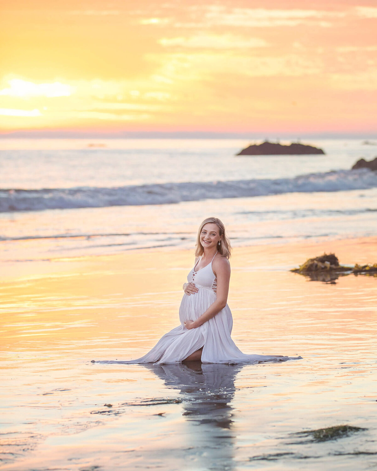 Maternity photoshoot at Malibu beach location by Los Angeles Maternity Photographer with new mom sitting on the sand with sun setting behind