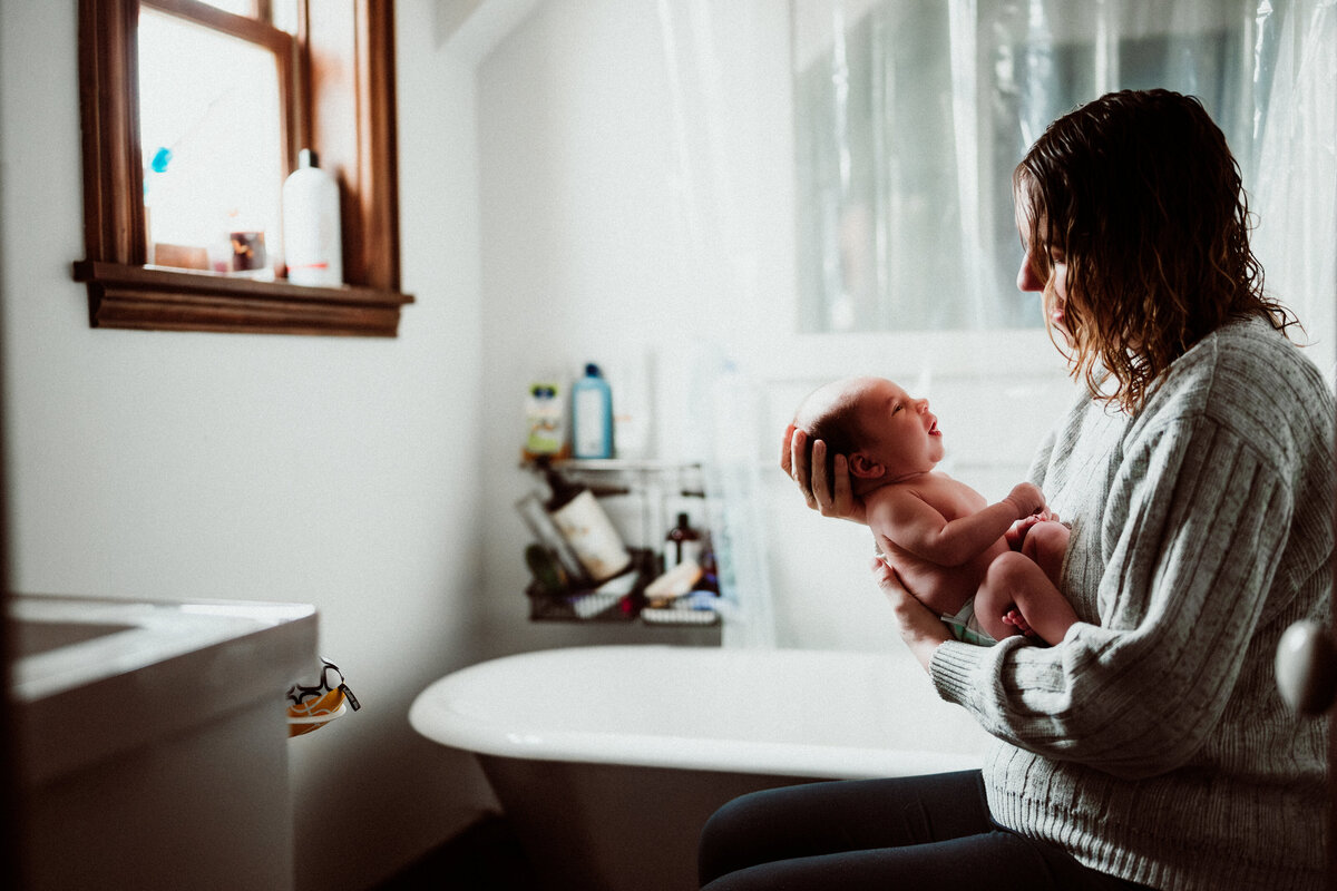 Newborn baby boy in a white onesie during an at-home lifestyle session in the Twin Cities.