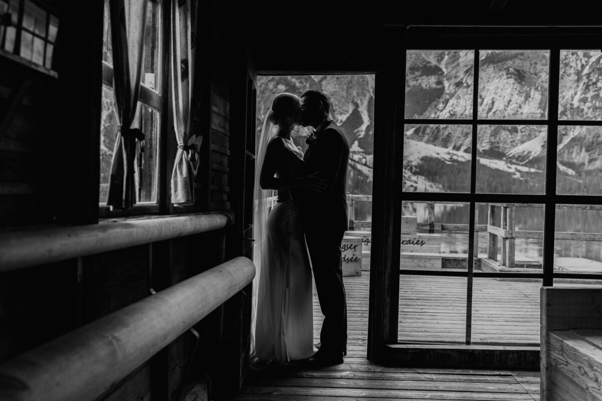 Black and white photo of couple kissing inside wooden boathouse