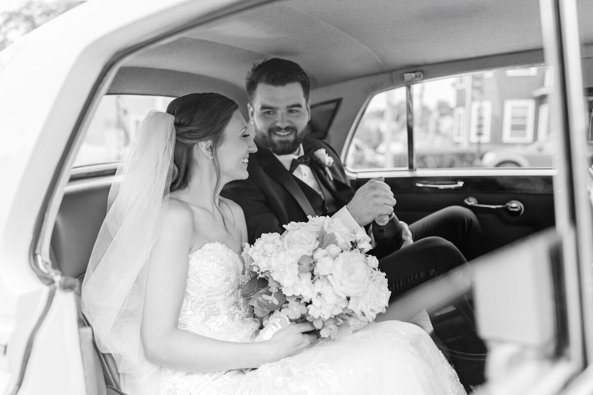 A bride and groom open a bottle of champagne in a Rolls Royce