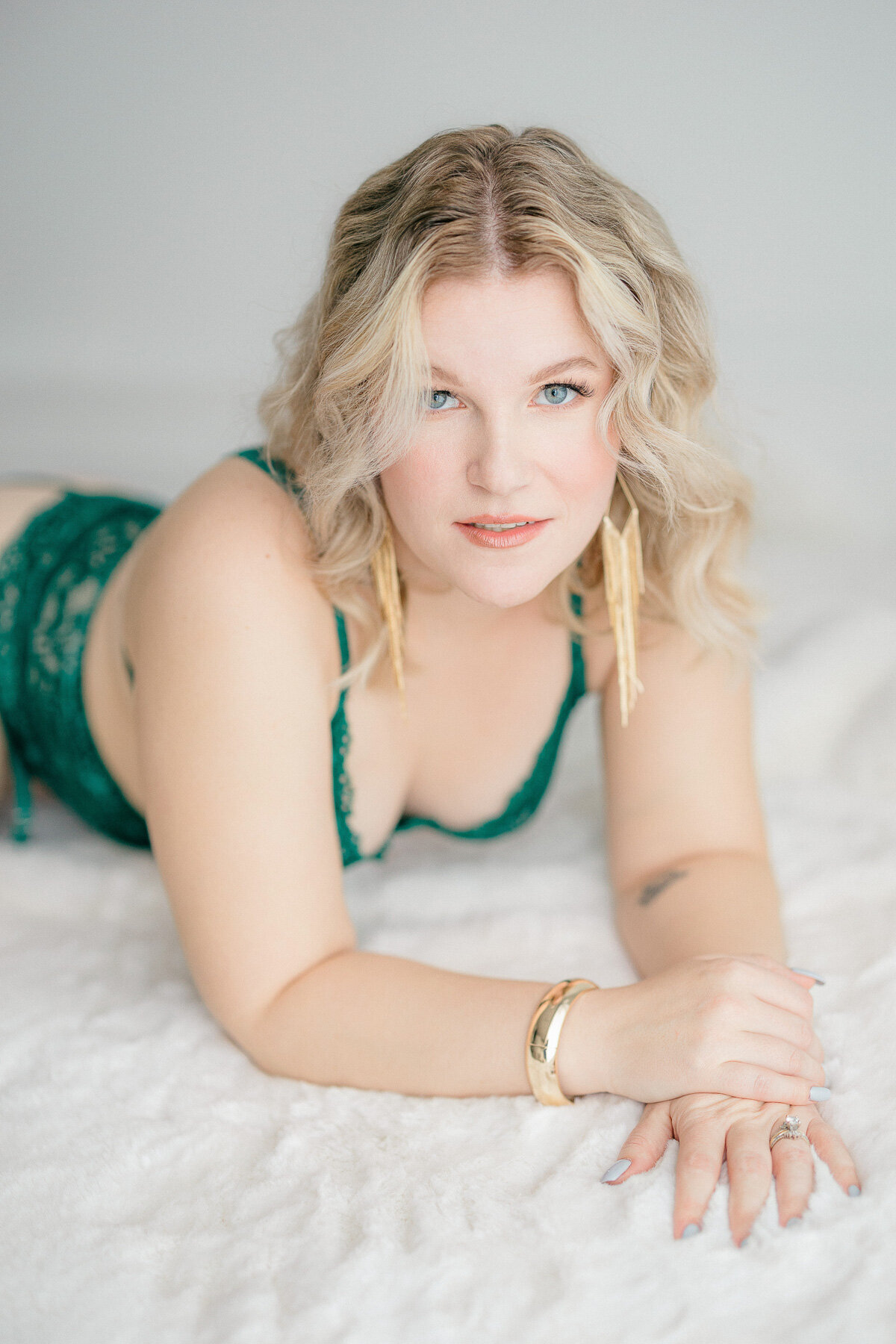 A woman in green lingerie lays on her stomach with her hands lying on top of each other and looks at the camera for her session with Indianapolis boudoir photographer, Brittney Lear.