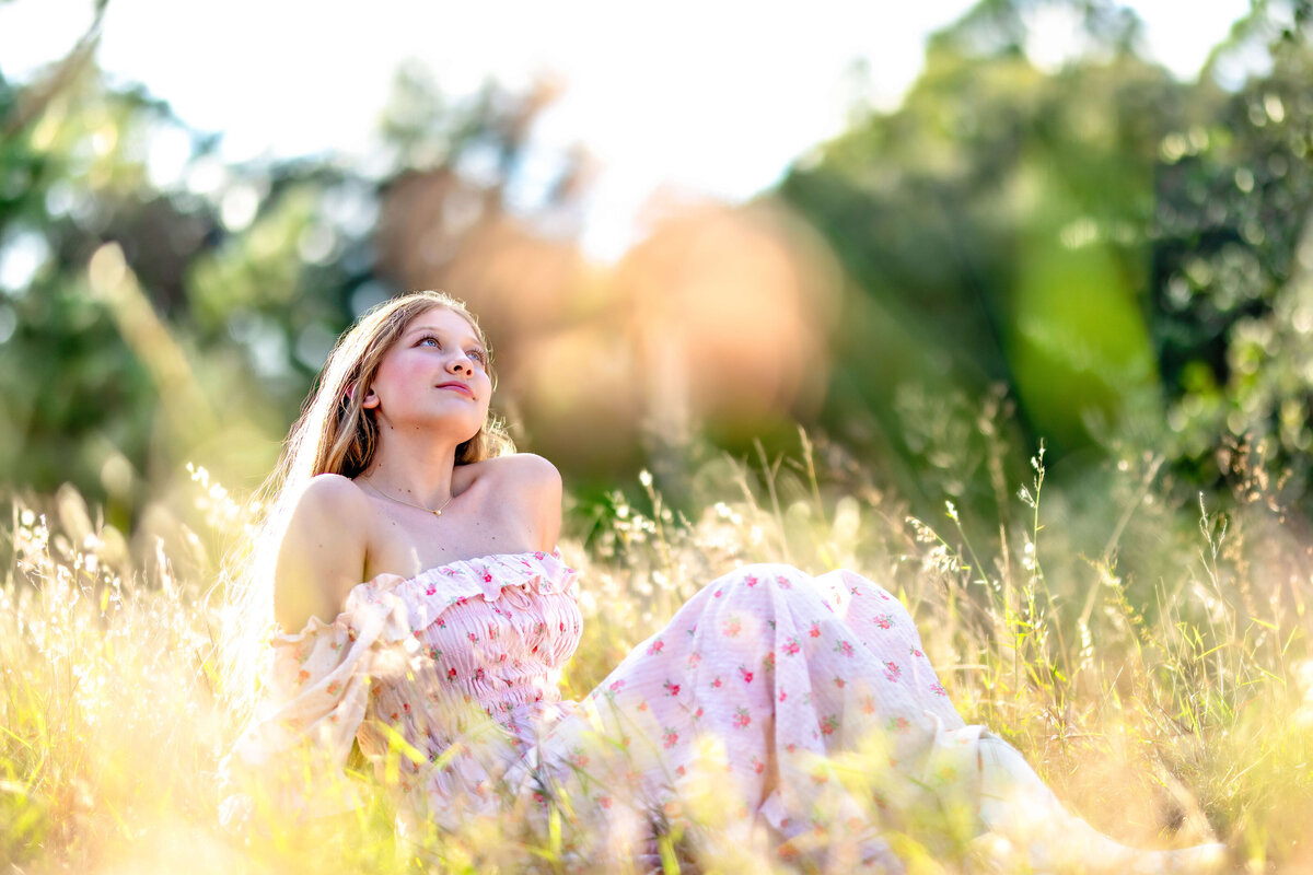 Senior girl in a pink floral dress sitting in golden grass during editorial-style session in Central Florida