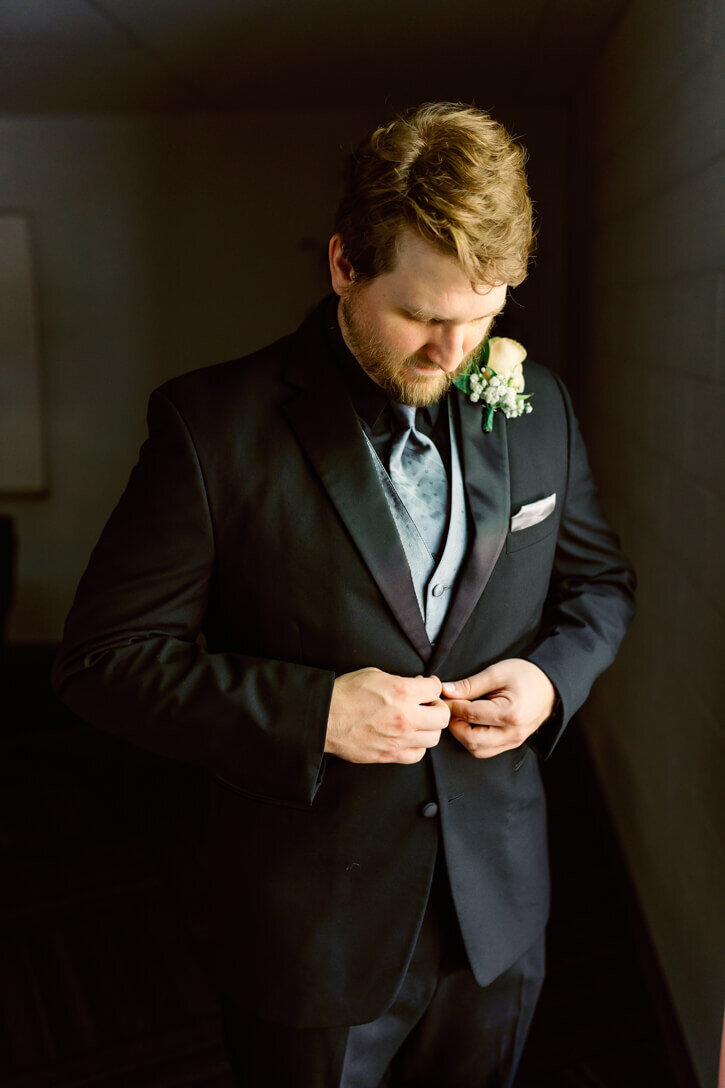 Groom buttoning his coat during groom prep on his wedding day before the ceremony.