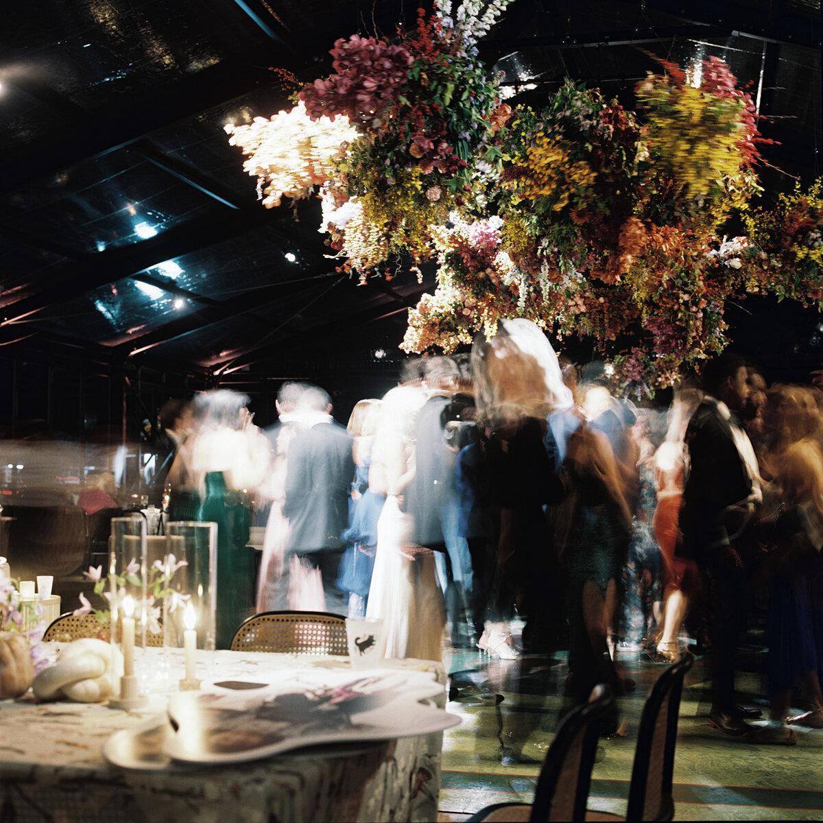 Interacting and sculptural floral clouds hang over the dance floor and bars of this fall wedding reception in Tennessee. Clear top tent build out for fall wedding reception in Tennessee hills.  Product clustered floral clouds in a tasteful fall color palette of copper, ruby, gold, burgundy, rust, and lavender. Orchids, bittersweet berries, butterfly ranunculus, and tulips are highlighted. Unique floral design with flower forward large scale installations. Design by Rosemary & Finch Floral Design in Nashville, TN.