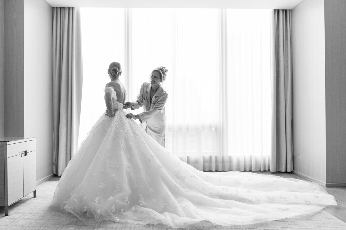A bride and her mother in black and white at the Four Seasons Hotel Toronto. The mother is helping her daughter zip into her wedding dress