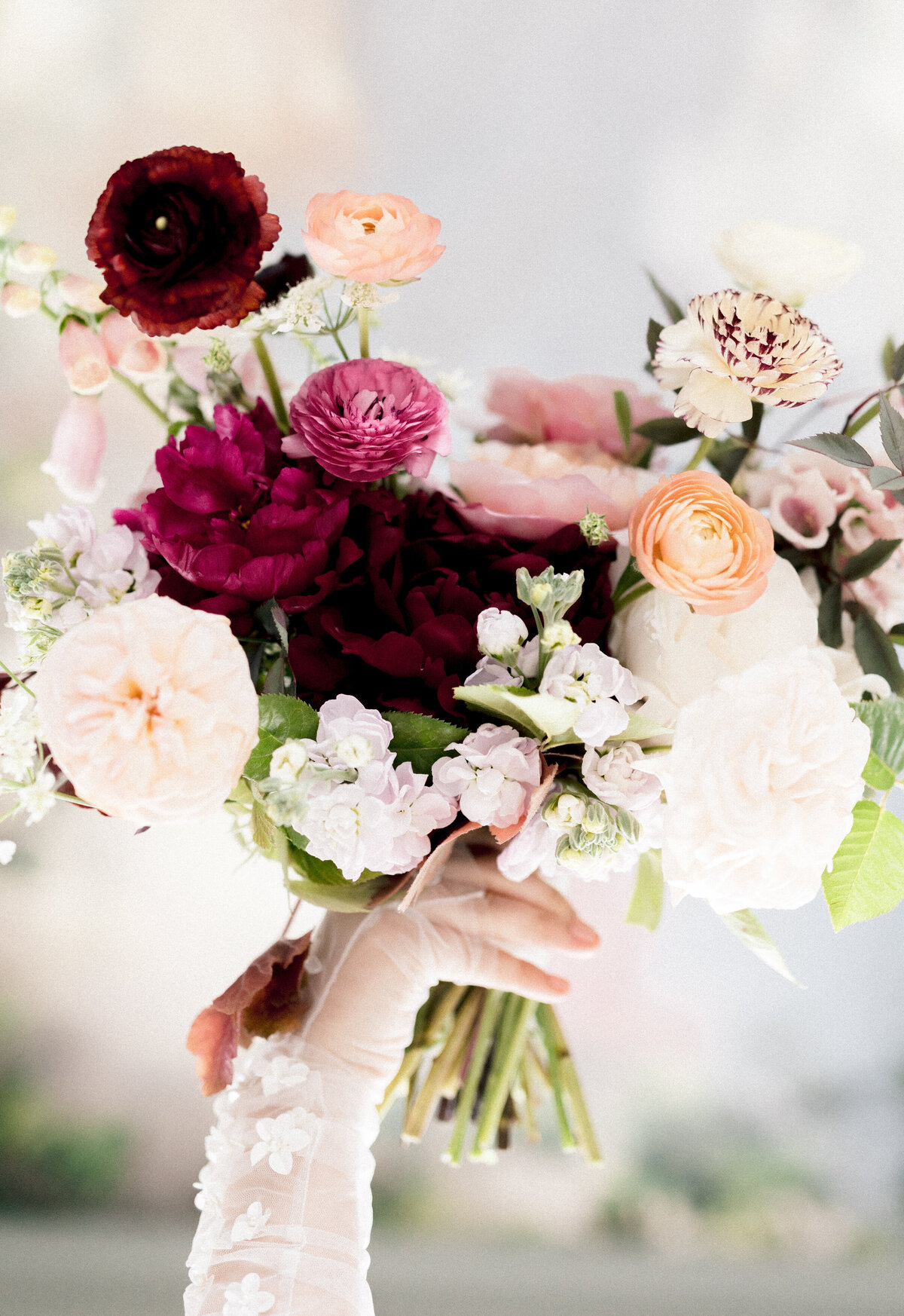 A bride's hand holding a beautiful bouquet of deep red and pink flowers.