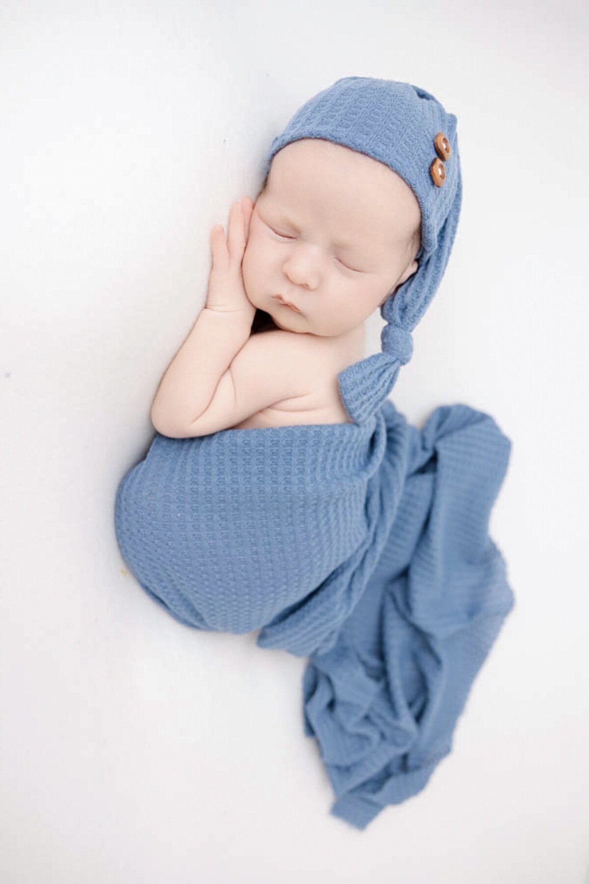 Baby boy wearing a blue sleepy hat and wrapped in a matching blue blanket.