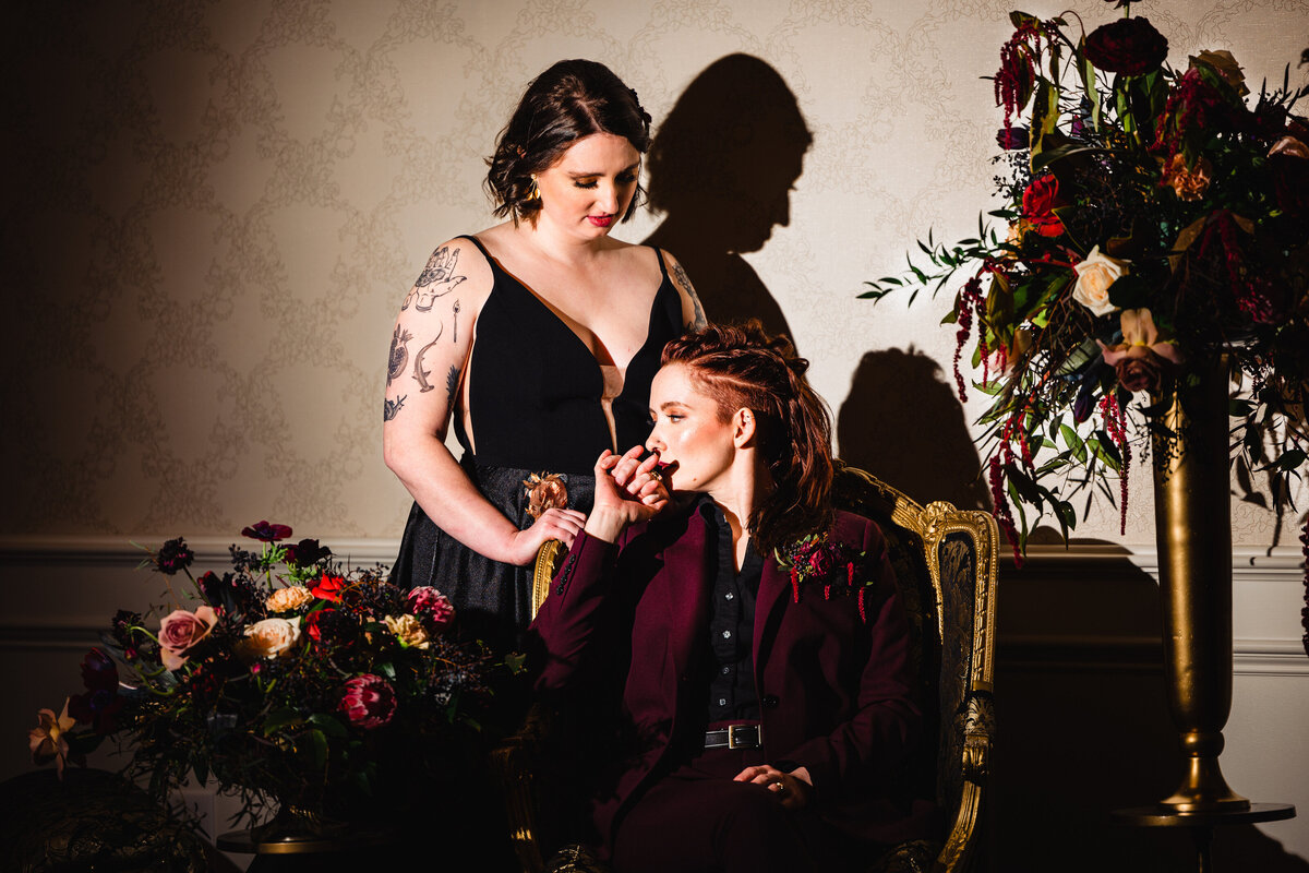 Bride in suit sitting while bride in black dress is standing