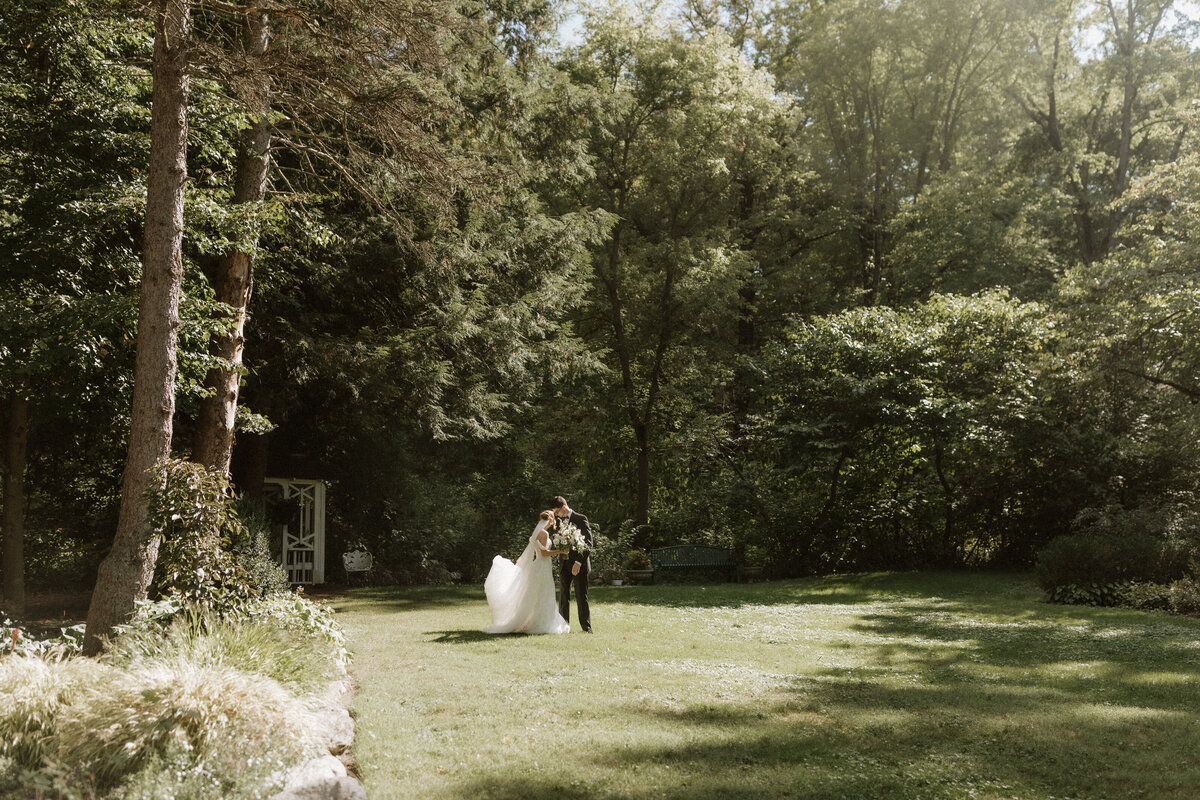 Bride and groom walking hand in hand through a sunlit garden during their outdoor wedding ceremony, photographed by Rainstorm Photo & Video in a warm, cinematic style.
