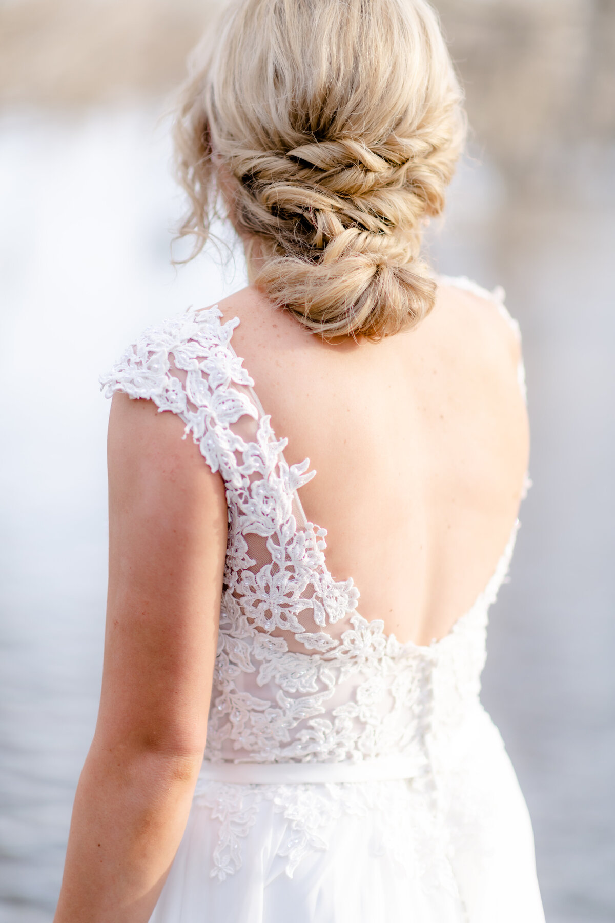detail shot of brides low back lace dress as the bride looks onto the lake