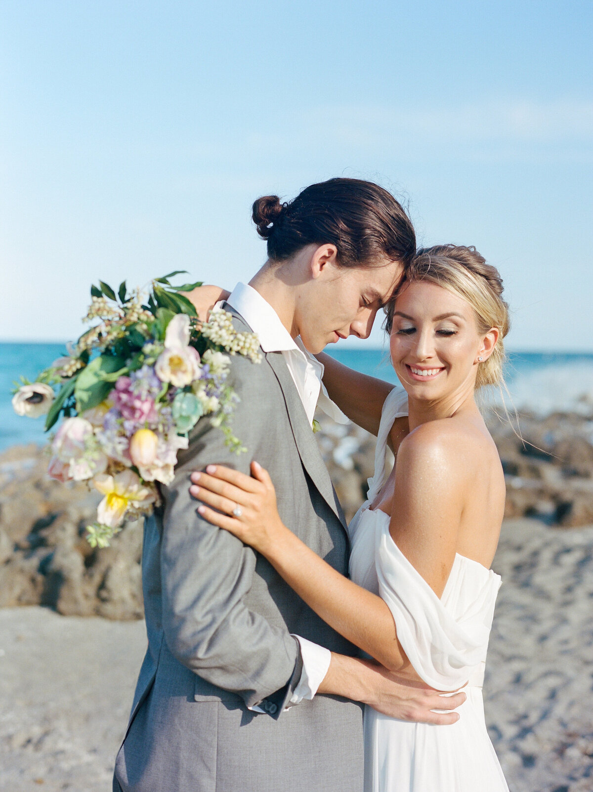 Bride and groom pose at beach.