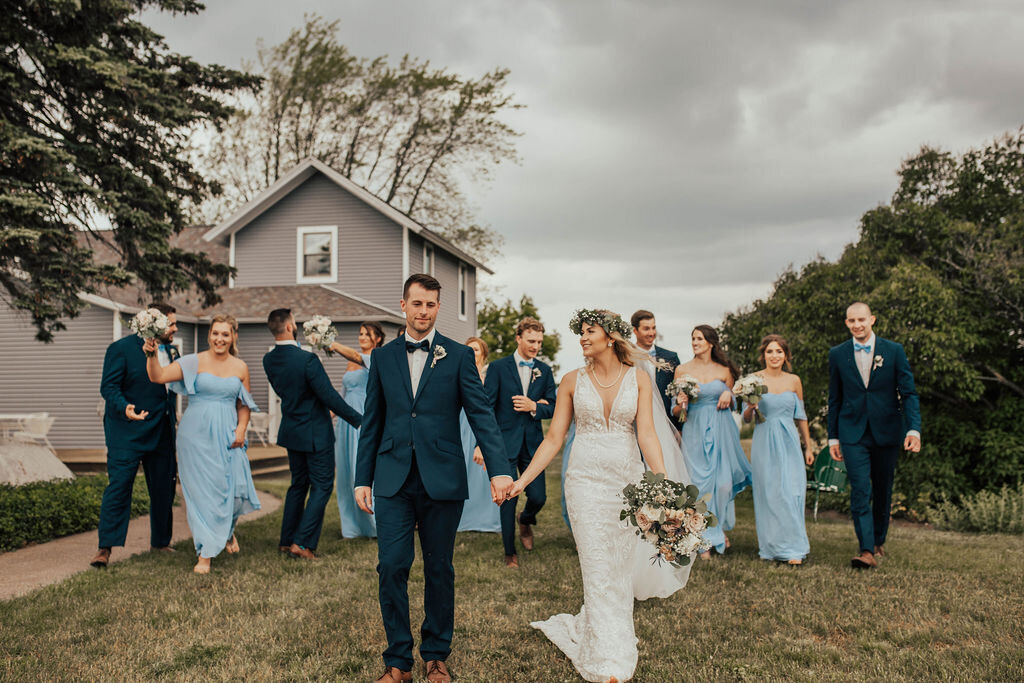 bride and groom holding hands walking together in front of their bridal party