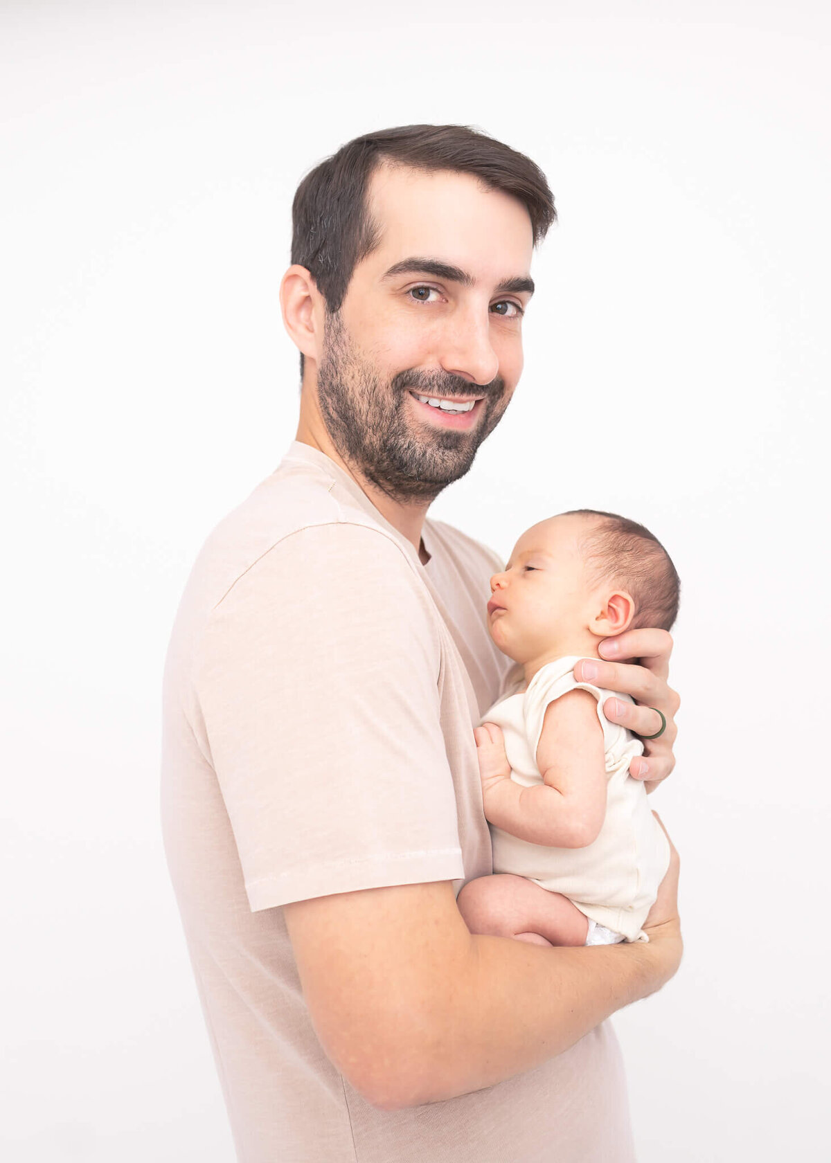 New father in studio portrait with new baby son both in beige on white backdrop