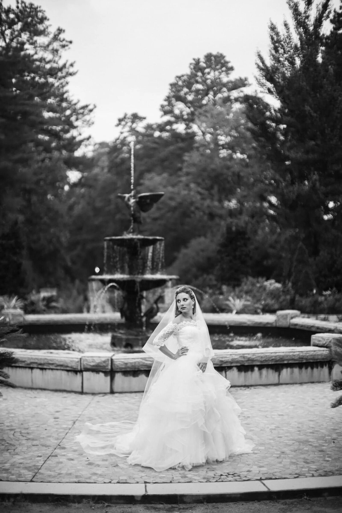 A bride standing in front of a fountain with one hand on her hip