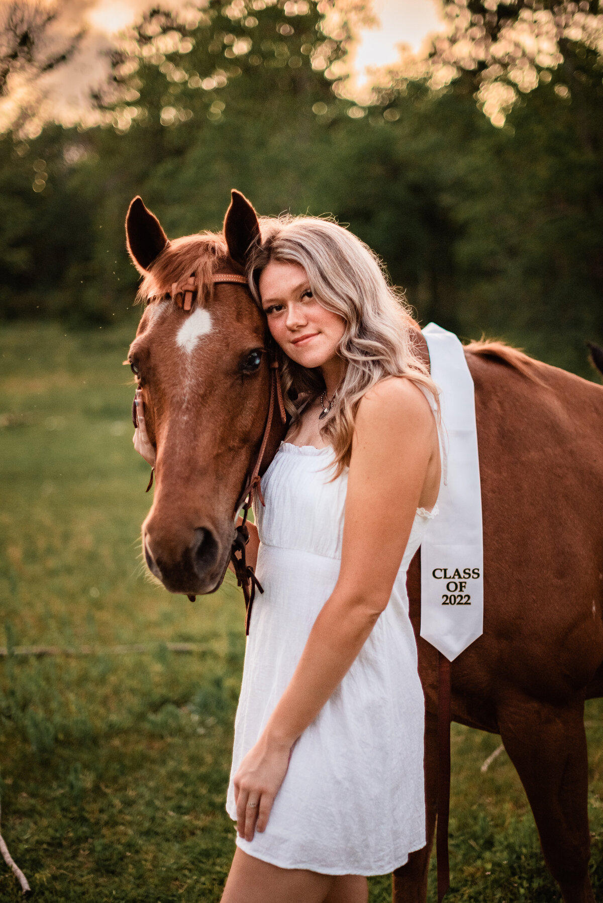 A Santa Fe High School graduate  hugs her horse in an open field at sunset.