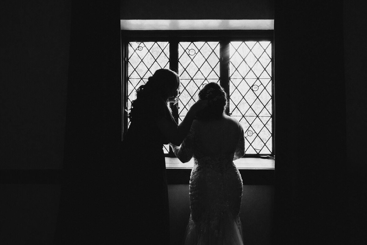 A silhouette of two people in dresses standing by a window