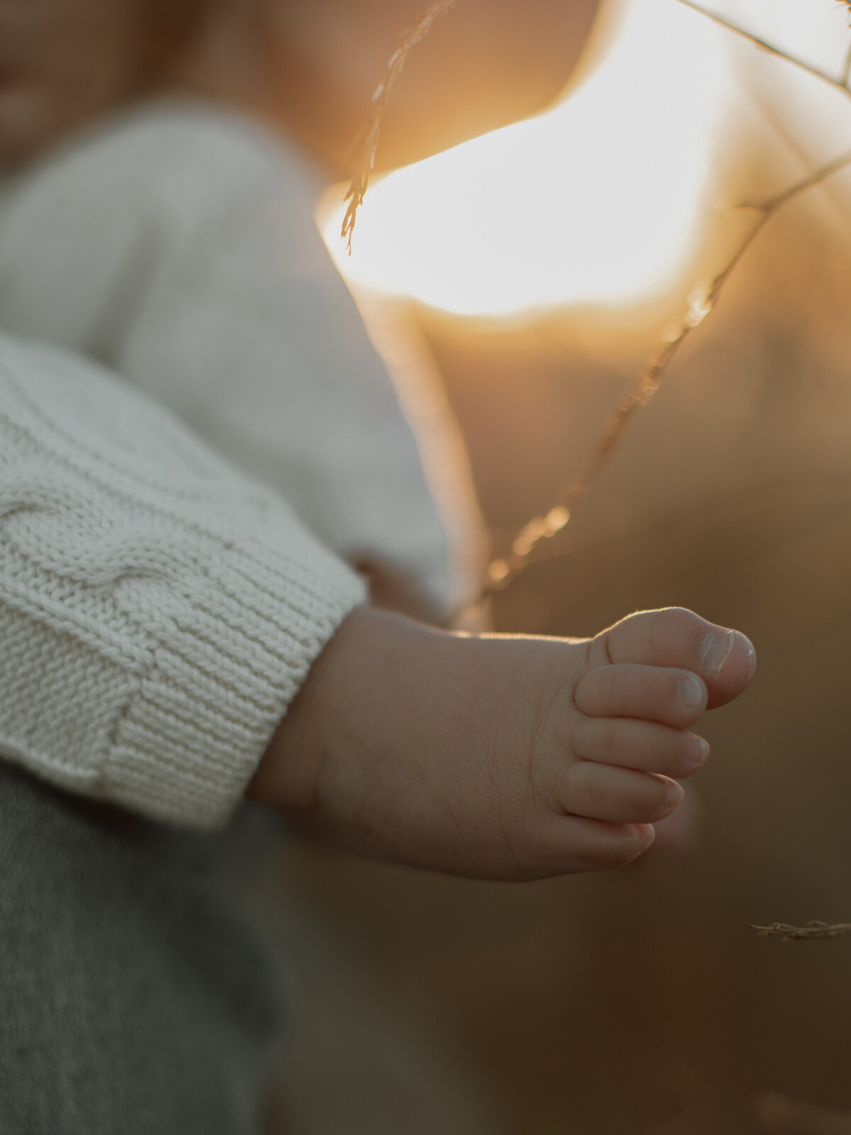 A close-up of baby's foot in an open field, the wind gently brushing past them.