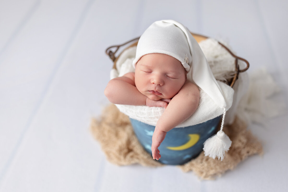 Newborn wrapped in blue sleeping inside a soft fluffy nest setup