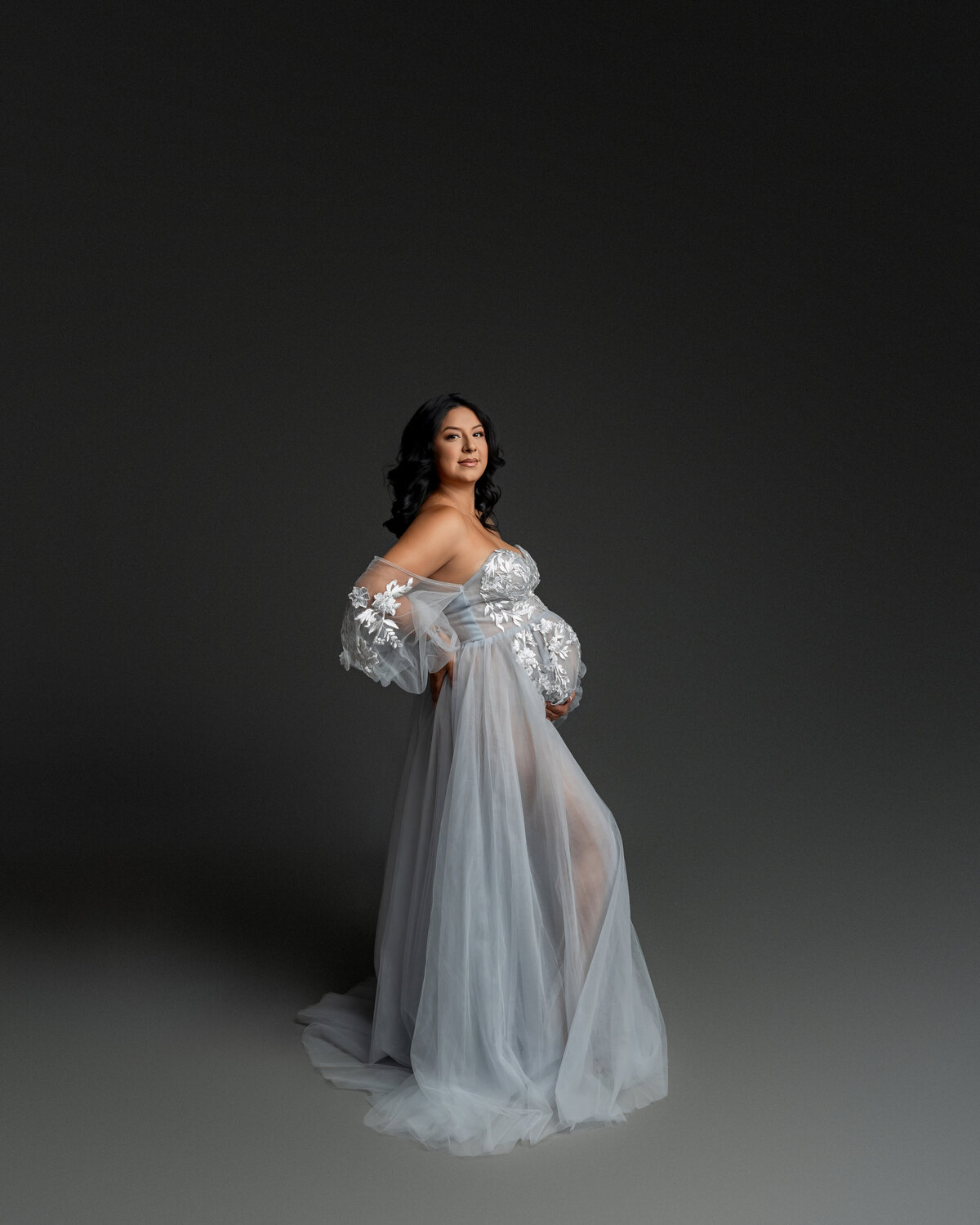 In a soft baby blue dress, a mother-to-be poses in profile, highlighting the graceful curves of her pregnancy. Captured by Inland Empire maternity photographer Kaitlyn Dawn Photography.